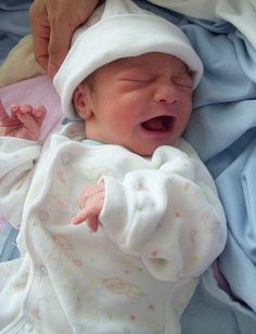 a baby in a white hat is yawning while being held by someone's hand