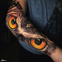 an owl's eye tattoo on the arm is shown with orange eyes and feathers