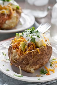 two white plates topped with baked potatoes covered in shredded cheese