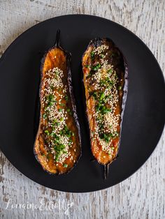 two stuffed eggplant halves on a black plate with sesame seeds and parsley