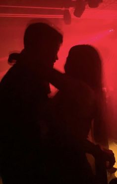 two people standing next to each other in front of a red light at a party