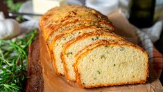 sliced loaf of bread sitting on top of a cutting board next to garlic and herbs