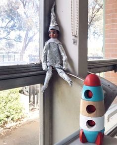 a toy rocket ship sitting on top of a window sill next to a doll