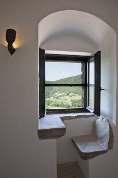 a window in a white wall with a view of the hills outside it and a bench on the floor