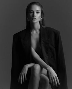 a black and white photo of a woman sitting on a stool with her legs crossed