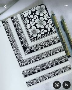 some black and white designs on a sheet of paper next to two markers, one with a pen