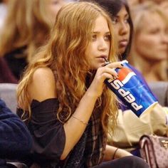 a woman sitting in the stands drinking from a can