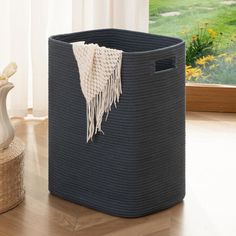 a blue basket sitting on top of a wooden floor next to a vase and window