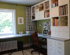 a home office with green walls and white bookcases on the desk, along with a window