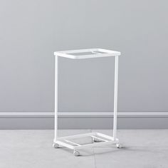 a small white cart with wheels on the floor in front of a gray wall,