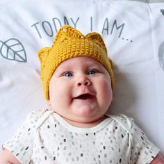 a baby wearing a yellow knitted hat laying on top of a white sheet with the words today i am written on it