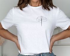 a woman wearing a white t - shirt with a dragonfly embroidered on it