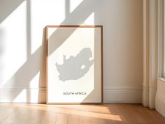 a white framed poster with the shape of south africa on it in an empty room