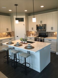 a large kitchen with white cabinets and counter tops, two stools at the island