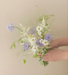 a person holding a bouquet of white and blue flowers with green leaves in their hands