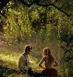 a man and woman sitting on the ground in front of trees