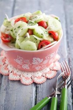 a pink bowl filled with cucumbers and tomatoes on top of a doily