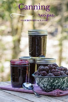 jars filled with jam sitting on top of a wooden table next to a bowl of berries