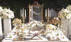 a table topped with lots of white flowers next to a tall mirror and vases