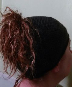 the back of a woman's head wearing a black hat with red hair in it