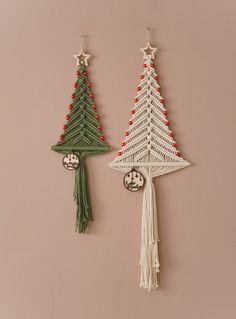 two crocheted christmas trees hanging from hooks on a pink wall next to each other