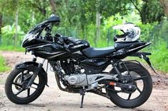 a black motorcycle parked on the side of a dirt road in front of some trees