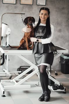 a woman standing next to a brown dog on top of a white table in a room