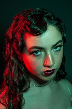 a woman with red light on her face and dark hair is posing for the camera