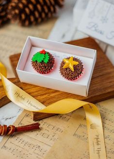 two decorated cupcakes sitting in a box on top of a piece of paper