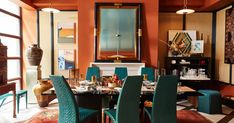 a dining room with orange walls and blue chairs around the table in front of an ornate mirror