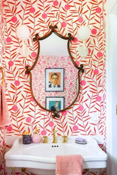 a bathroom with pink and orange wallpaper, gold faucet, white sink and mirror