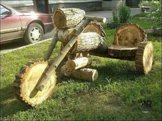 a wooden log car is sitting in the grass next to a red car and tree stumps