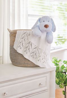 a blue stuffed animal sitting on top of a white dresser next to a basket and window