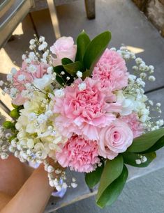 a bouquet of pink and white flowers sitting on top of a wooden chair next to a person