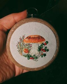 a hand holding a small cross stitched mushroom with flowers and leaves on it's side