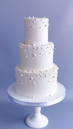 a three tiered white wedding cake with pearls on it