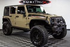 a beige jeep parked in a garage with checkered flooring and large tires on it