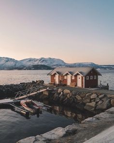 a boat is docked in the water next to some small red houses with snow covered mountains in the background