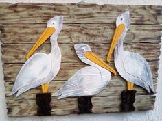 two white pelicans are standing on wooden planks, one is painted yellow and the other is gray