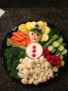 a black plate topped with cauliflower, carrots and broccoli covered in a clown face