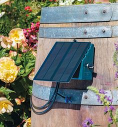 a solar panel attached to the side of a wooden barrel with flowers in the background