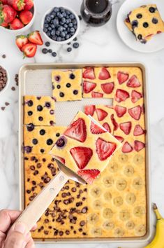 someone is cutting strawberries into squares on a tray with bananas and blueberries in the background