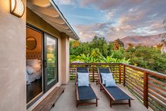 two chaise lounge chairs on a balcony overlooking the trees and mountains at sunset or dawn