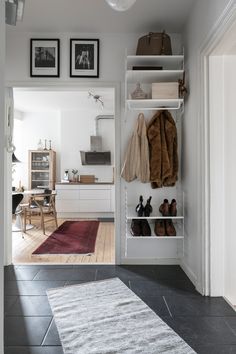 an open closet with shoes and coats hanging on the wall, next to a rug