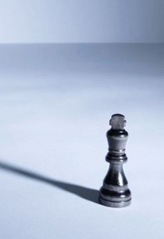 a black and silver chess piece on a white surface with a long shadow from the pawn