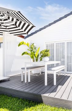 a white table and chairs under an umbrella on a wooden deck in front of a house