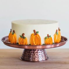 a cake decorated with pumpkins and leaves on a metal platter sitting on a wooden table