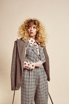 a woman with blonde hair is posing for a photo wearing plaid pants and jacket, holding a brown bag