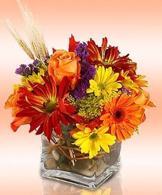 a vase filled with lots of colorful flowers on top of a glass table next to an orange wall