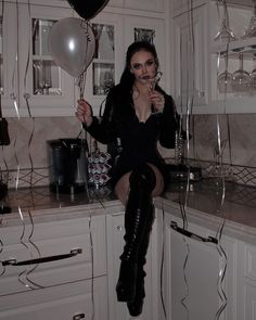 a woman sitting on top of a counter next to balloons and wine glasses in the air